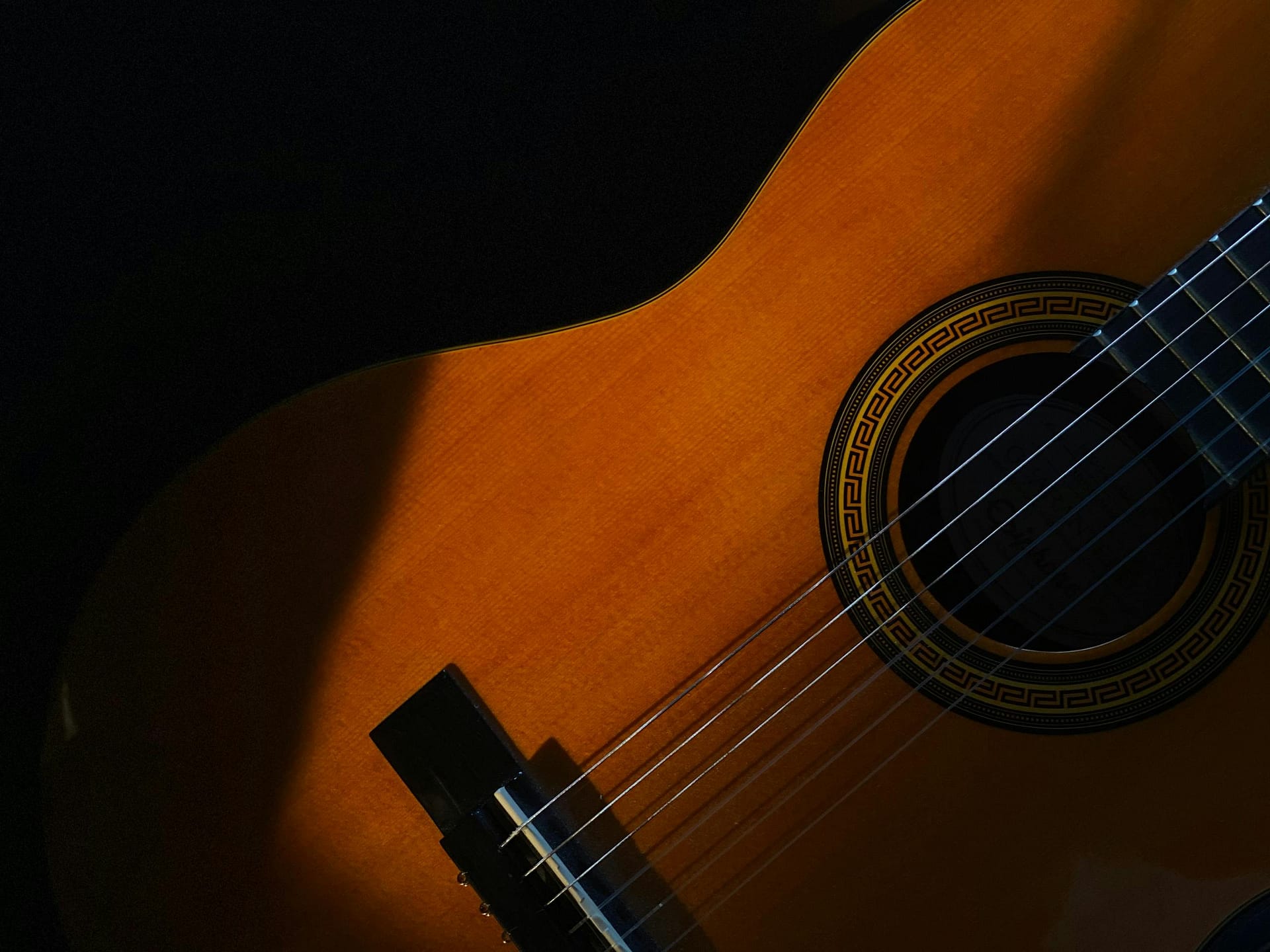 Artistic close-up photo of an acoustic guitar highlighting the wooden body and strings in shadow.